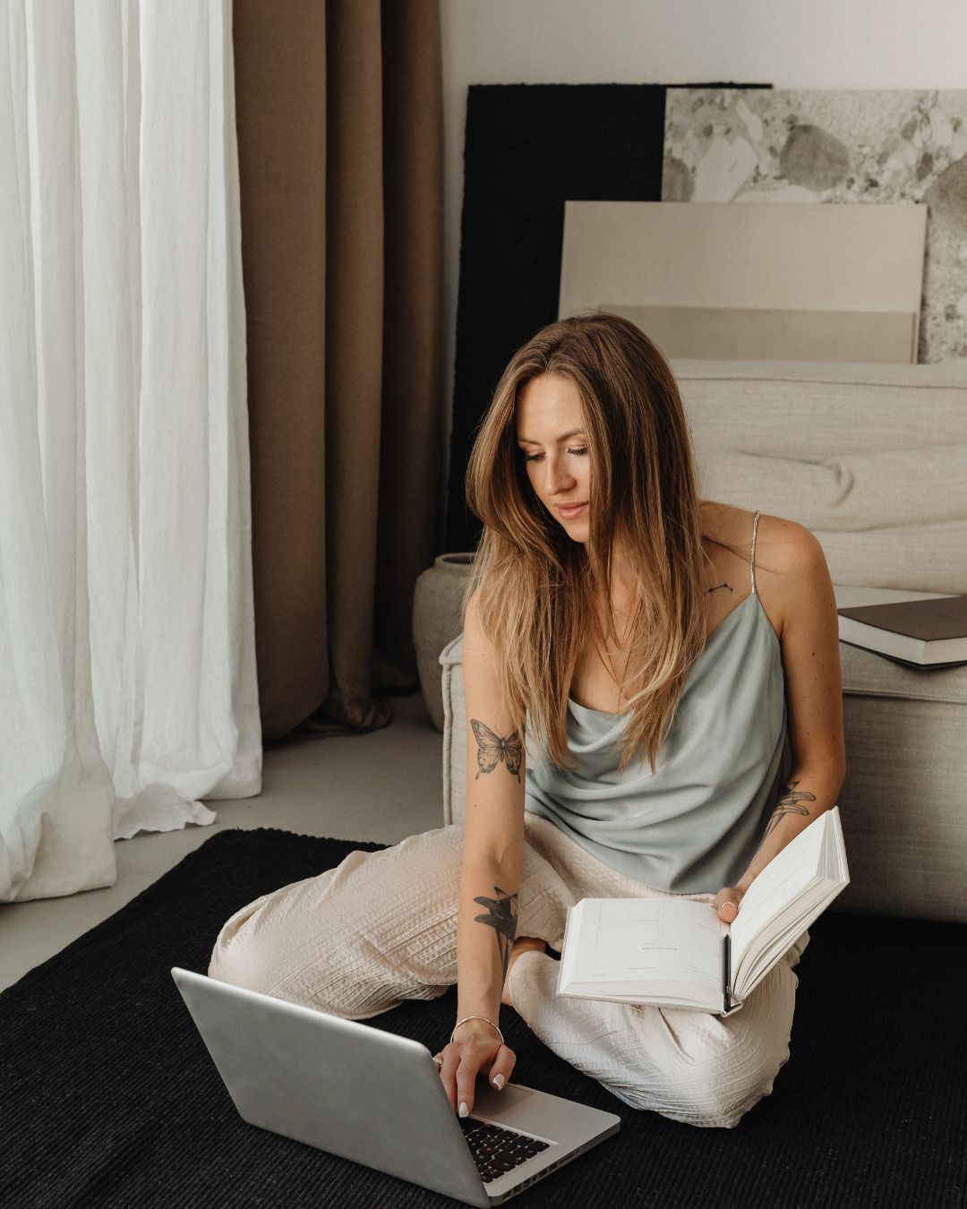 Marie sitzt barfuß mit Laptop und Notizbuch auf einem Teppich.