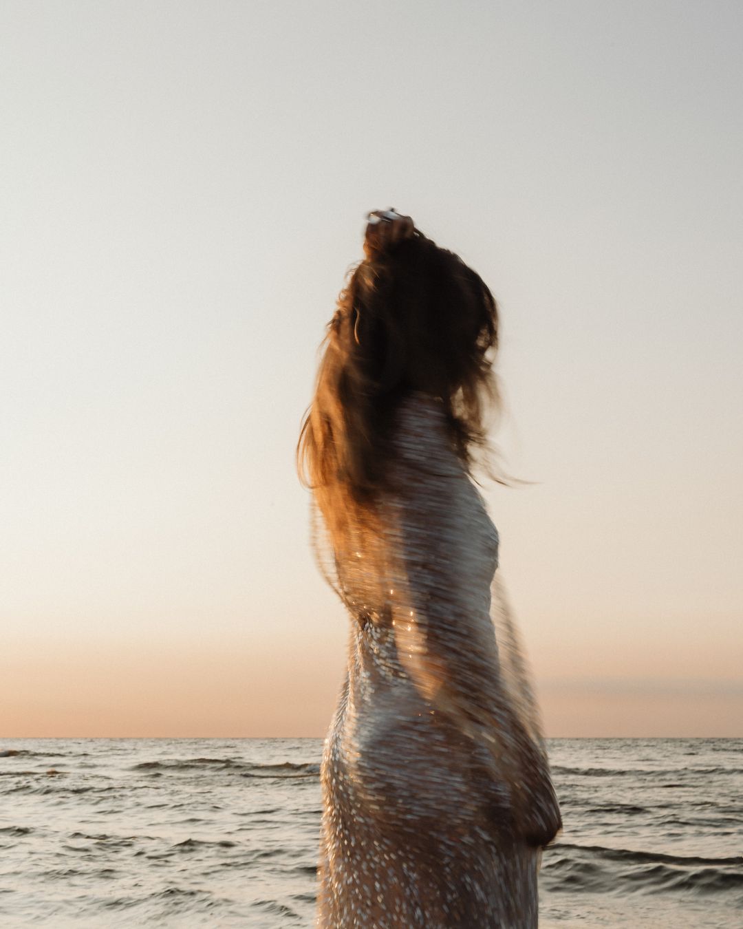 Marie steht am Meer, ihr schimmerndes Kleid und ihr Haar bewegen sich im Wind.