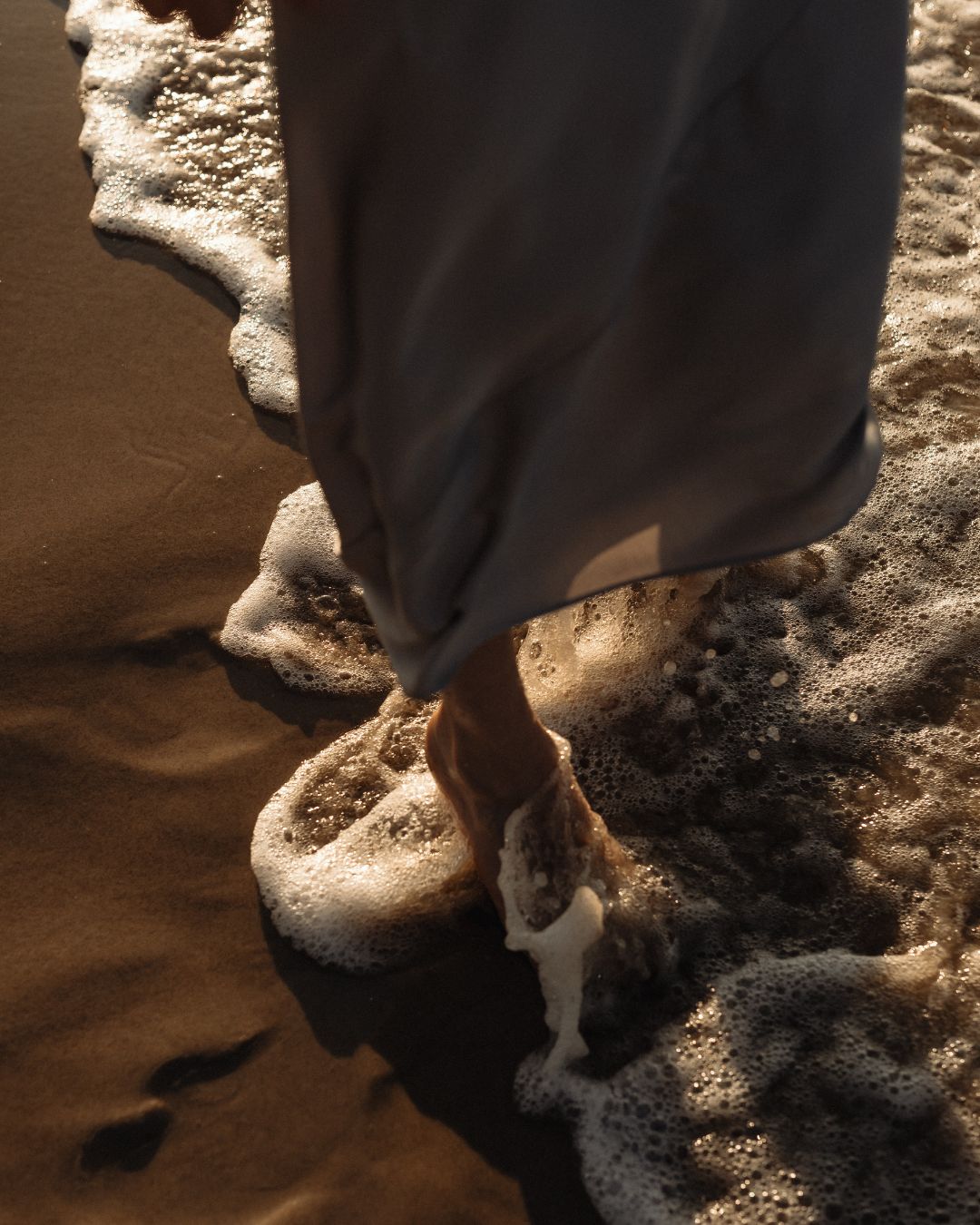 Marie läuft barfuß durch das Wasser am Strand.